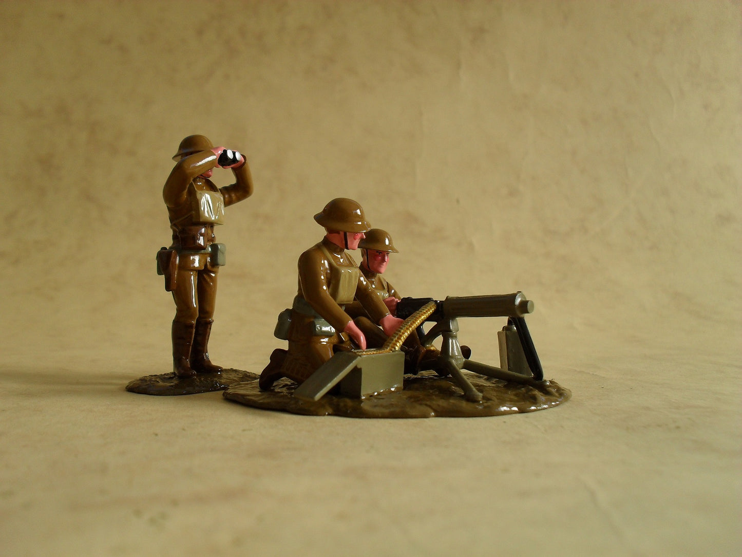 Toy soldier set featuring an American Vickers machine gun crew during World War I. The set includes three figures: one officer standing and observing through binoculars, and two crew members seated at the Vickers machine gun. The figures are dressed in period-appropriate military uniforms with steel helmets. They are positioned on a small, muddy terrain base, capturing a moment of intense focus and preparation for action.