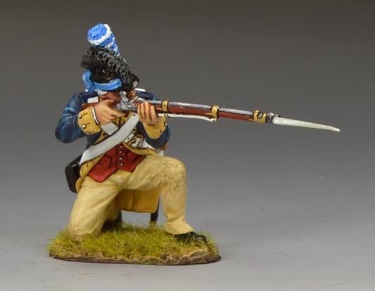 A miniature figurine of a kneeling soldier in 18th-century military uniform aims a musket with fixed bayonet, set on a grassy base. The soldier wears a blue coat, tan pants, and a tall hat with a blue-and-white plume.