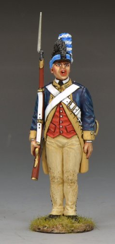 A toy soldier figurine of a Revolutionary War soldier stands at attention, wearing a blue and red uniform with tan trousers, white crossbelts, and a tall black hat with a blue plume, holding a musket upright by his side.