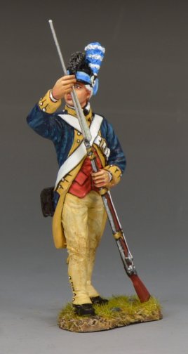 A detailed toy soldier figurine of an 18th-century soldier in a blue and yellow uniform, holding a rifle upright with one hand and saluting with the other, stands on a small grassy base against a plain background.