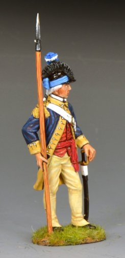 A model toy soldier figurine dressed in an 18th-century military uniform with a blue coat, red vest, yellow trousers, and a black hat, holding a spear, stands on a small grassy base against a plain background.