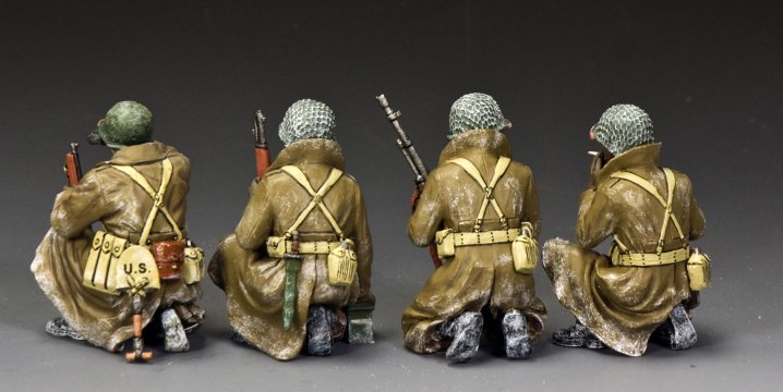 Four toy soldiers in military uniforms with backpacks and rifles on a gray background