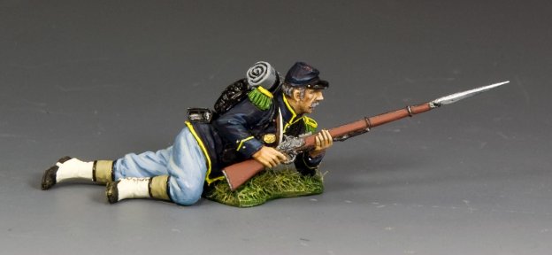 King and Country's "Lying Ready" features a military miniature toy soldier in a blue uniform, prone on grass and aiming a rifle with bayonet, complete with backpack and hat for an authentic historical look.