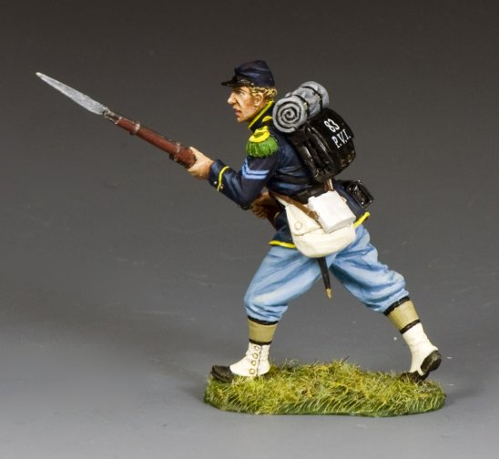 A painted figurine of a Union Civil War soldier in blue uniform and light blue pants, holding a rifle with a bayonet, marching forward on a grassy base with a backpack and bedroll.
