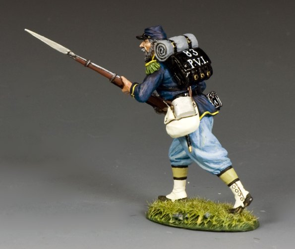 A painted toy soldier in a blue Civil War uniform with a backpack and bedroll, holding a rifle with a bayonet, is posed in a running stance on a grassy base.