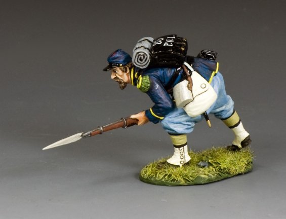 A painted figurine of a Civil War soldier in a blue uniform crouches forward with a bayonet rifle, backpack, and bedroll, posed on a grassy base against a plain background.