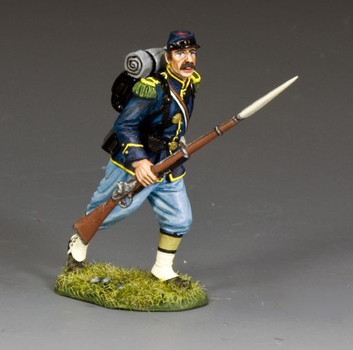 A miniature toy soldier in a blue Civil War-era uniform runs forward, holding a rifle with a bayonet. He has a mustache, a backpack, and stands on a grassy base.