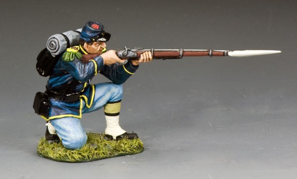 A painted military miniature figurine of a Union soldier in a blue Civil War uniform is kneeling on grass, aiming a rifle with a bayonet attached. 