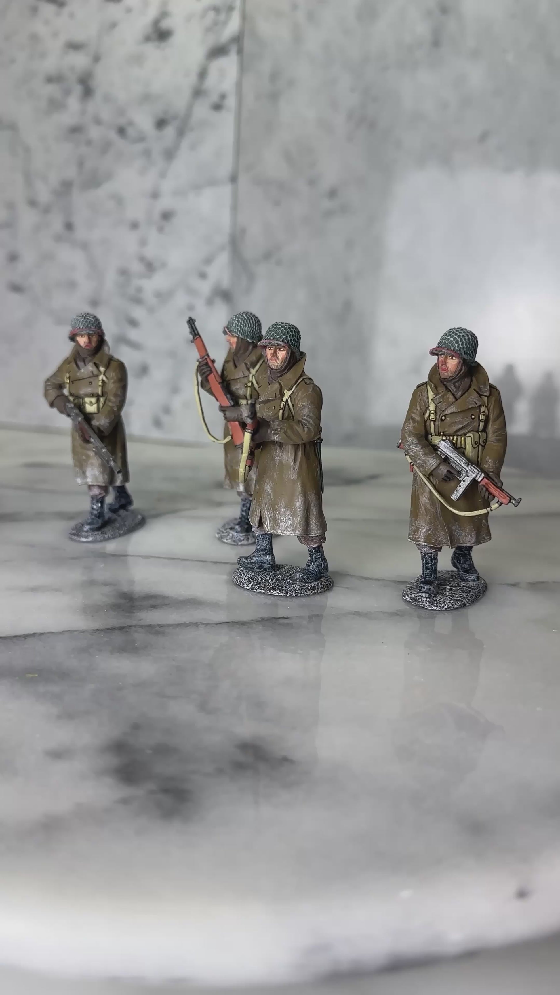 360 view of King & Country BBA100 four-figure set of a U.S. infantry patrol advancing through snow in winter overcoats — an NCO with a Thompson, two riflemen with M1 Garands, and a BAR gunner.