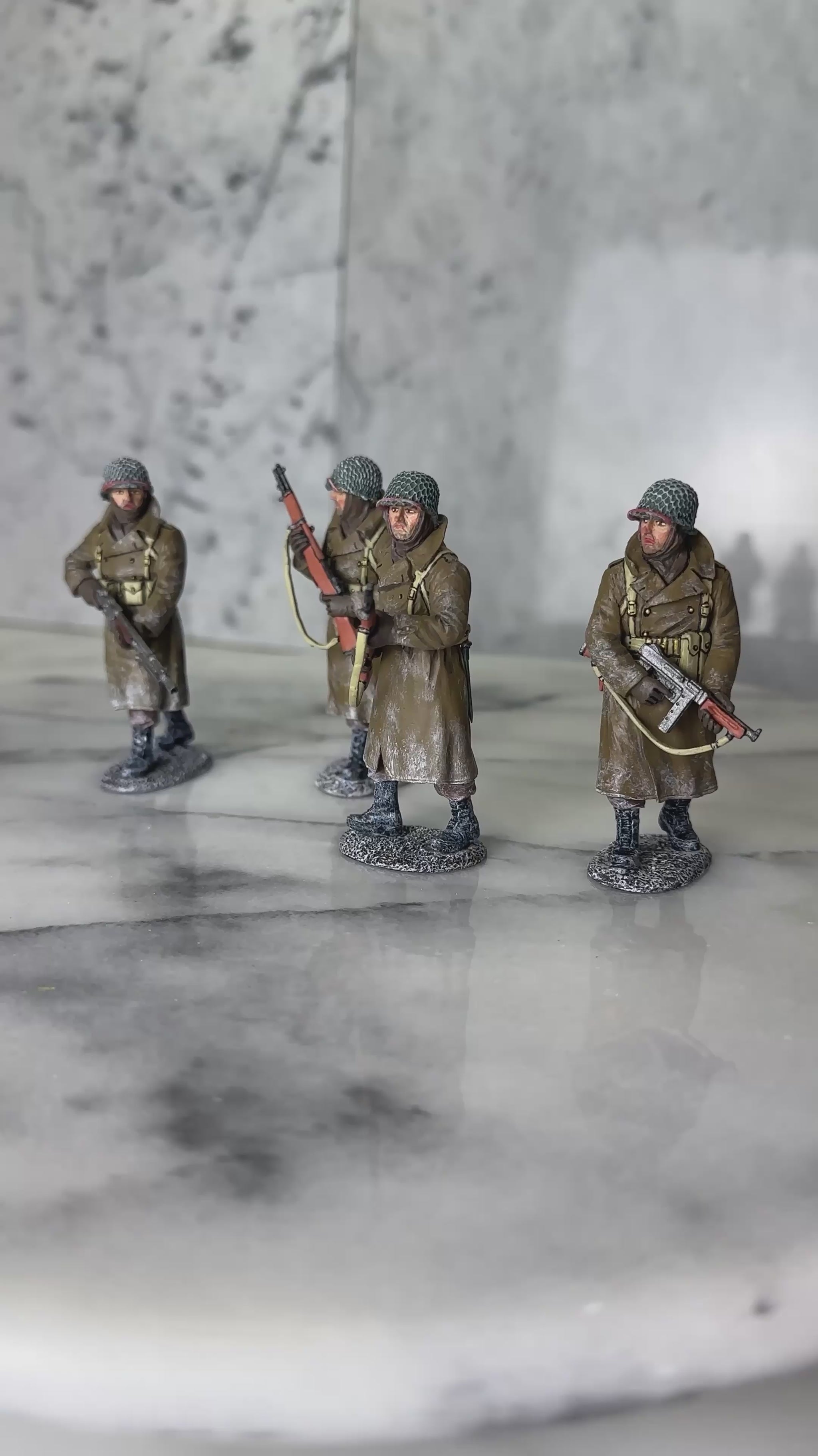360 view of King & Country BBA100 four-figure set of a U.S. infantry patrol advancing through snow in winter overcoats — an NCO with a Thompson, two riflemen with M1 Garands, and a BAR gunner.