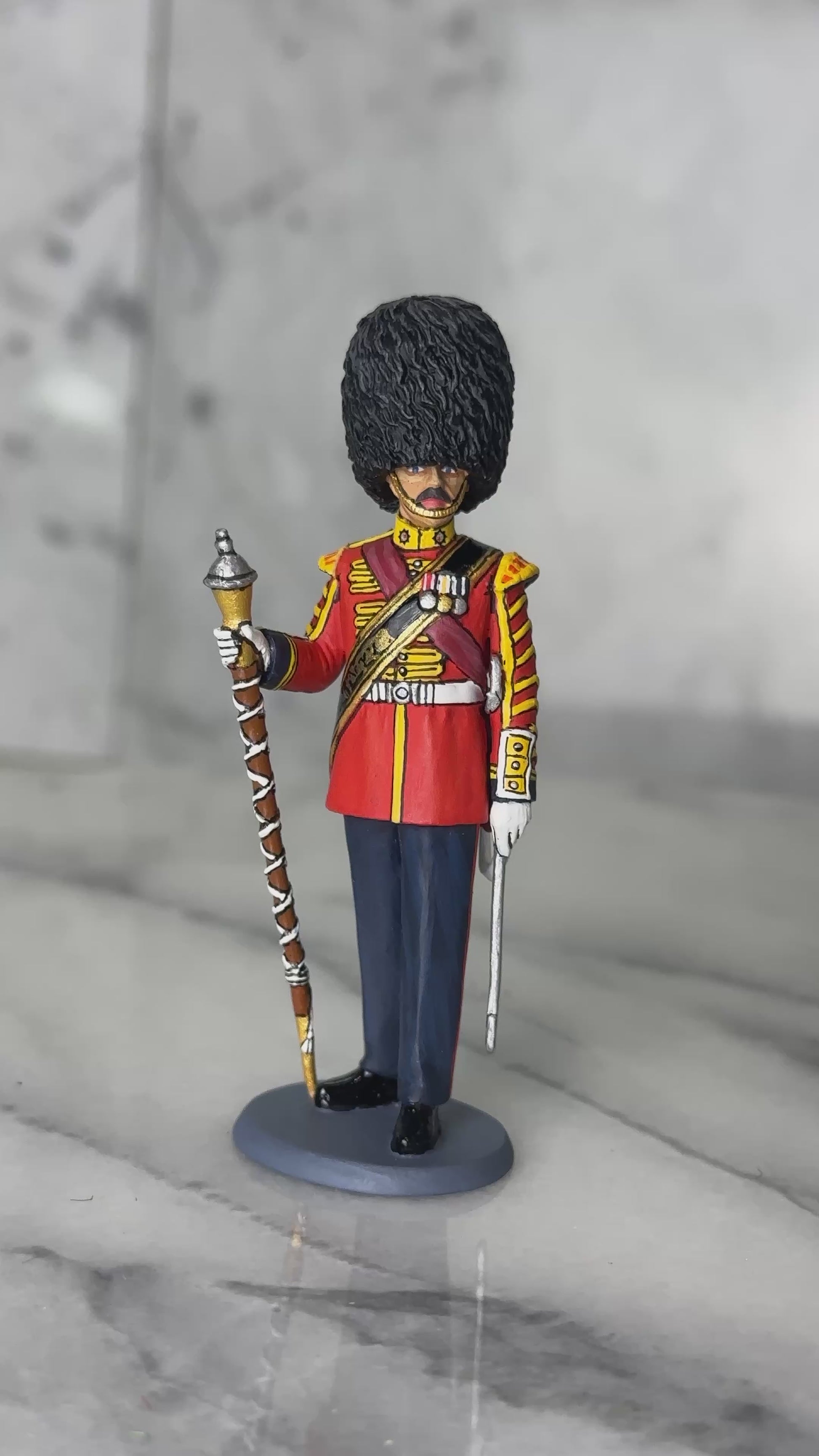 360 view of toy soldier King & Country Scots Guards Drum Major — 1/30 scale matte-painted figure in ceremonial scarlet with gold lace, red sash, and bearskin cap, holding mace. Catalog CE122.