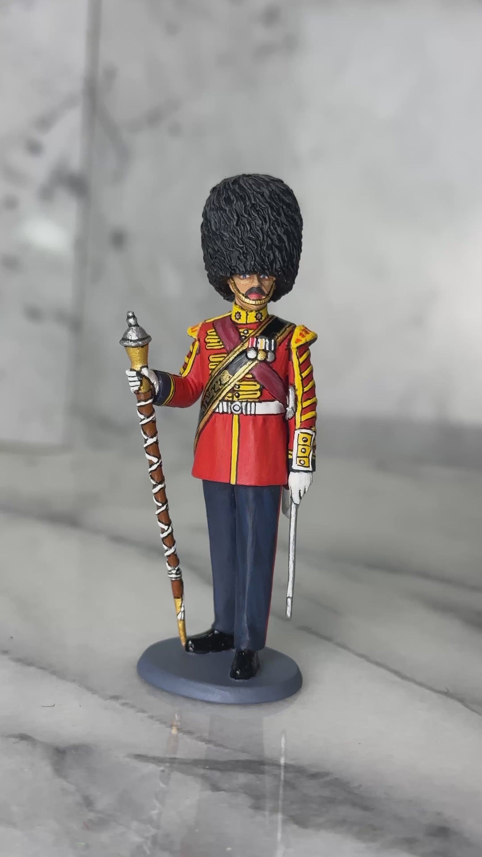 360 view of toy soldier King & Country Scots Guards Drum Major — 1/30 scale matte-painted figure in ceremonial scarlet with gold lace, red sash, and bearskin cap, holding mace. Catalog CE122.