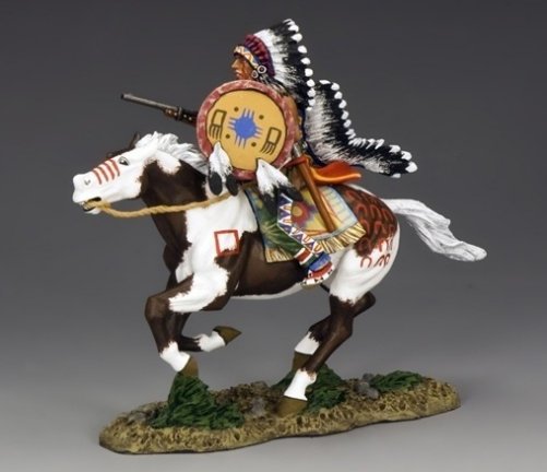 A painted figurine of a Native American warrior in a feathered headdress riding a galloping brown and white horse, holding a rifle, with decorated clothing and horse accessories.