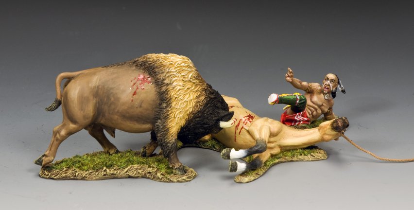 A painted figurine scene shows a bison attacking a fallen horse while a Native American man in colorful clothing and a feather headdress falls backward, appearing startled or injured, on a grassy base.