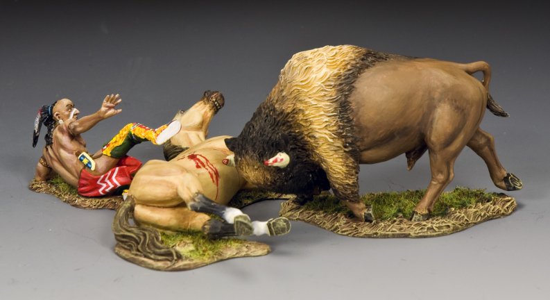 A military miniature painted figurine scene shows a bison attacking a fallen horse while a Native American man in colorful clothing and a feather headdress falls backward, appearing startled or injured, on a grassy base.