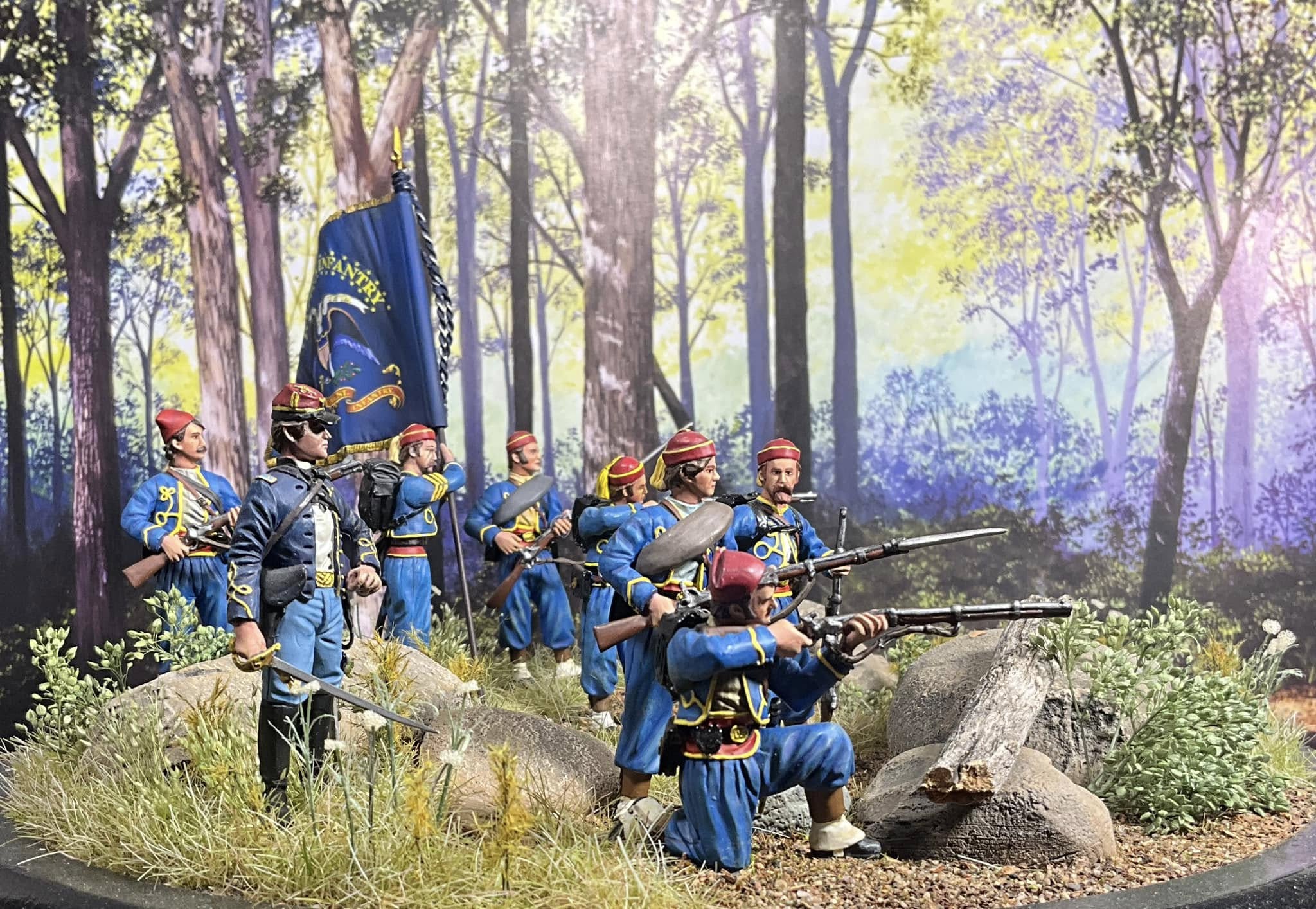 Model soldiers in blue uniforms with rifles in a forest setting