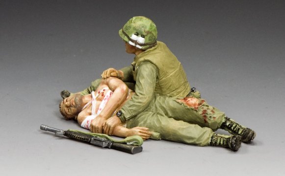 Taking Care of a Buddy. Model figure of a soldier in green uniform attending to a wounded person on a gray background