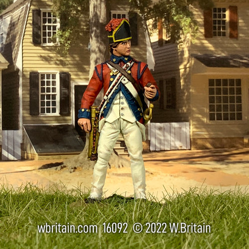 Collectible toy soldier miniature standing in white uniform and red jacket. He is standing in front of a house.