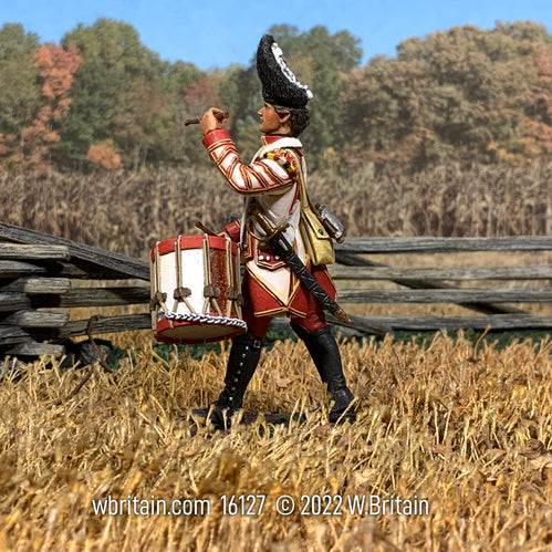 Collectible toy soldier miniature marching in a field while playing a drum.